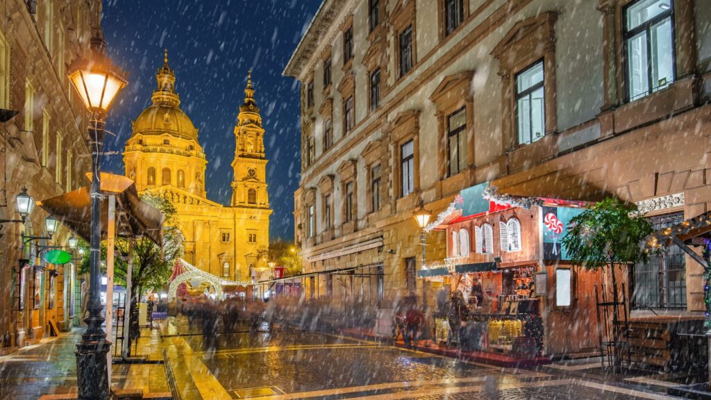 Sninganti Budapešto gatvė naktį su apšviesta bazilika ir kalėdinės mugės nameliu