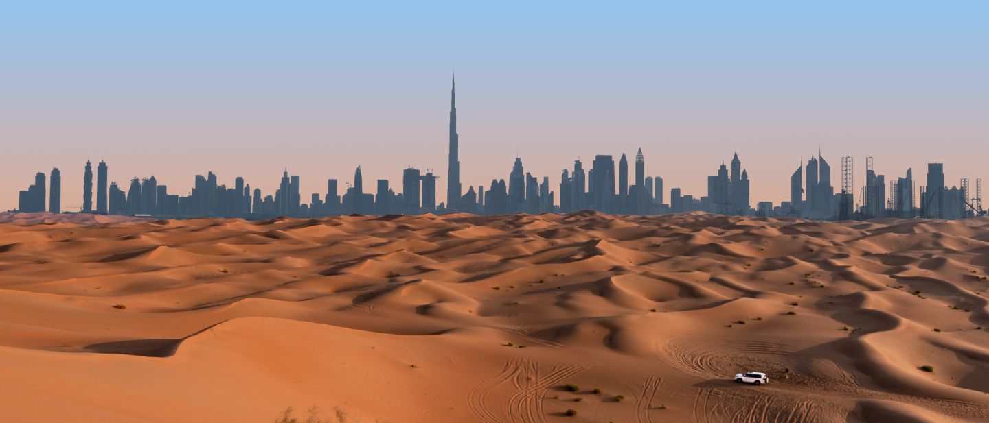 Baltas visureigis smėlio kopose ir modernaus miesto dangoraižių panorama Jungtiniuose Arabų Emyratuose