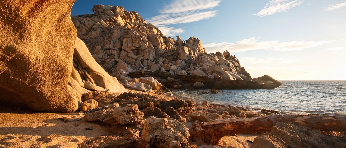 Auksinės uolos ir akmenys Sardinijos pakrantėje prie ramios jūros saulėlydžio metu