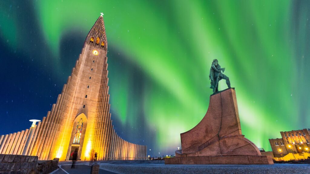 Apšviesta Hallgrímskirkja bažnyčia ir paminklas po ryškia žalia šiaurės pašvaiste nakties danguje