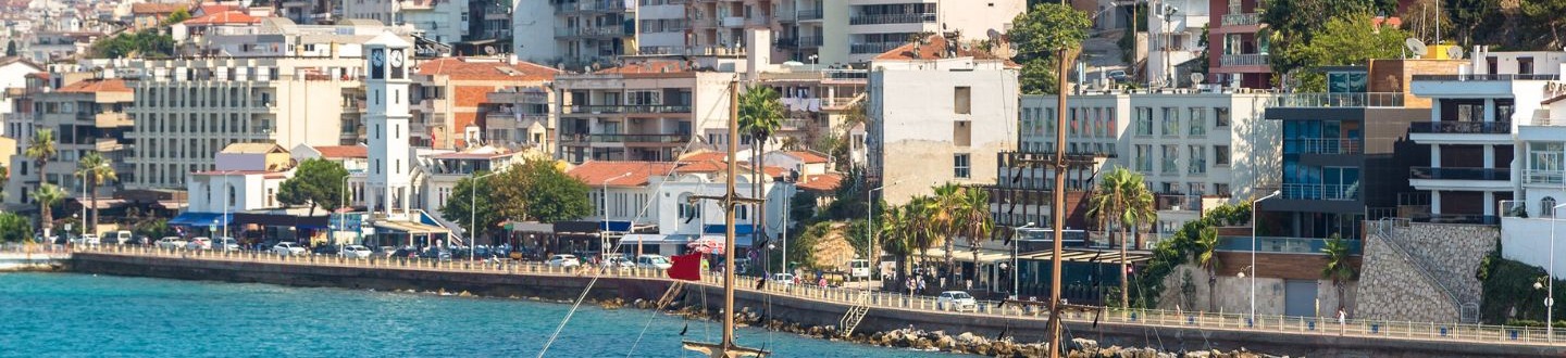 Medinis turistinis laivas plaukia žydra jūra šalia tankiai užstatytos Kušadasio pakrantės