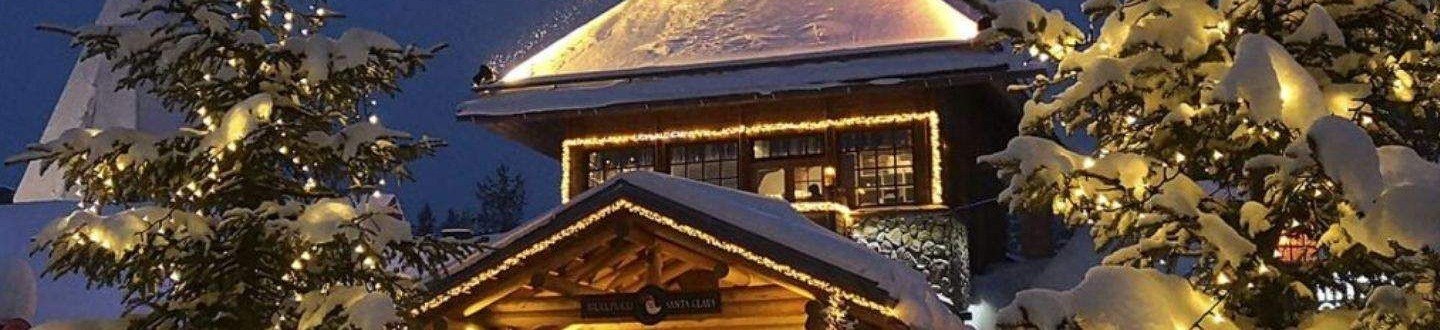 Apšviestas medinis pastatas su smailiu stogu ir papuoštos eglės snieguotoje Laplandijoje naktį