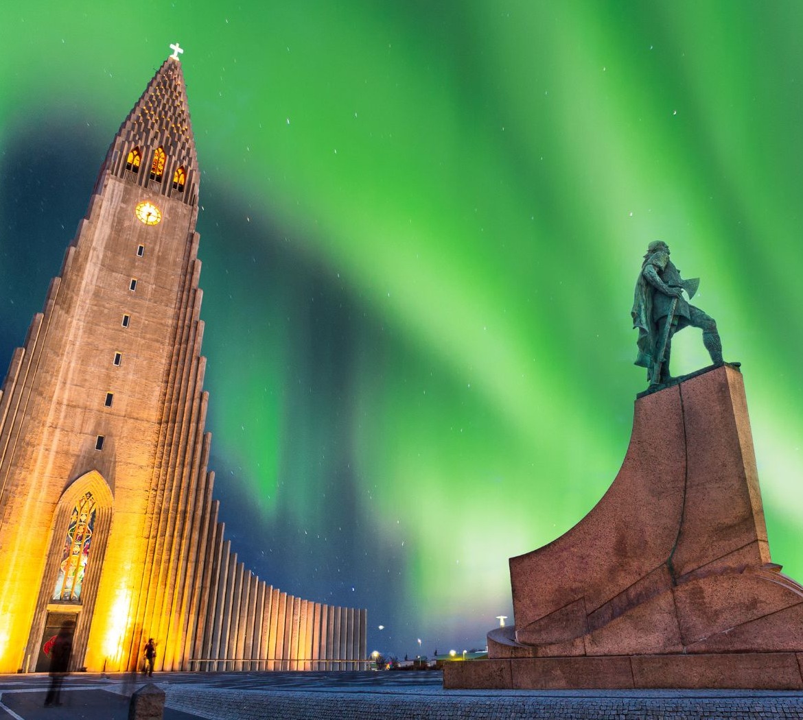 Apšviesta Hallgrímskirkja bažnyčia ir paminklas po ryškia žalia šiaurės pašvaiste nakties danguje